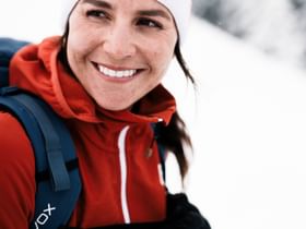 Eine Frau in Winterbekleidung der Marke Ortovox lächelt in die weisse Berglandschaft. 