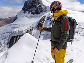 Ein Mann steht am Grat eines verschneiten Gipfels auf Ski und blickt in die Berglandschaft