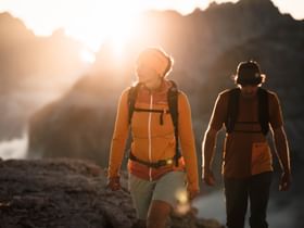 Eine Frau und ein Mann wandern im Sonnenuntergang in Ortovox Bekleidung in einer alpinen Bergwelt
