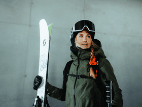 Eine Frau steht in Scott Skibekleidung und mit Scott Freerideski in einer Seilbahnstation