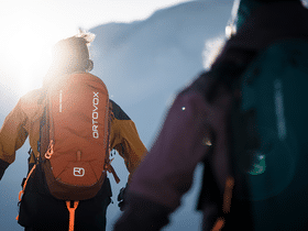 Zei Tourengeher laufen auf Tourenski mit einem Ortovox Rucksack einen Berg hinauf