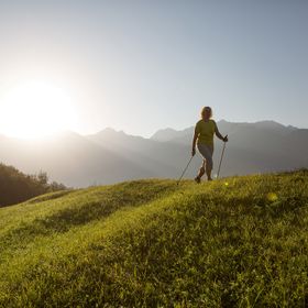 Eine Frau walked mit Stöcken in einer sommerlichen Wiesenlandschaft in Serfaus