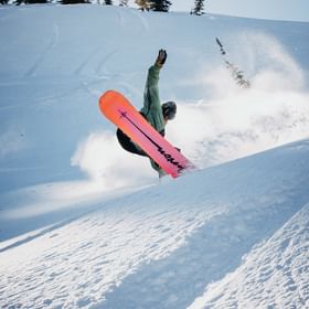 Ein Mann springt über eine Kante mit einem Burton Snowboard in einer weissen Winterlandschaft in den Bergen