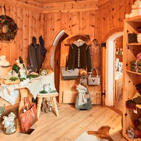 Holzschrank mit verschiedenen Wohnaccessoires und Souvenirs dekoriert im Geschäft Bsundrix. An der Wand hängen Trachtenjacken und Trachtenhüte