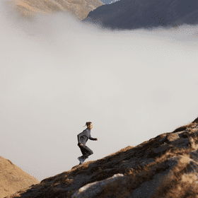 Eine Frau läuft in einer Berglandschaft einen Berg in On Bekleidung und Schuhen hoch