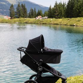 Summit Kinderwagen mit Babyschale auf einer Wiese im Hintergrund sind der Högsee, das Seeufer und Berge