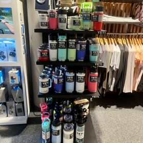 Eine große Auswahl an funktionaler Bekleidung und vielen anderen Accessoires wie die Trinkflaschen, Boxen von Yeti in vielen verschiednenen Farben dekoriert an einer Wand im Check In Bikecenter Serfaus
