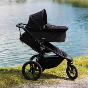 Summit Kinderwagen mit Babyschale auf einer Wiese im Hintergrund sind der Högsee, das Seeufer und Berge