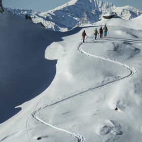 Eine Gruppe von Skifahrern geht an einem sonnigen Wintertag eine Bergtour einen tiefverschneiten Berghang hinauf