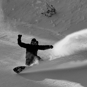 Ein Snowboarder macht mit seinem Snowboard im tiefen Schnee im Gelände einen riesigen Spray