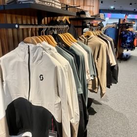 Eine große Auswahl an funktionaler Bekleidung und vielen anderen Accessoires zum Radfahren für Herren dekoriert an einer Wand im Check In Bikecenter Serfaus