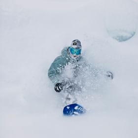 Ein Mann fährt in verschneiter Berglandschaft im Tiefschnee mit einem Snowboard 