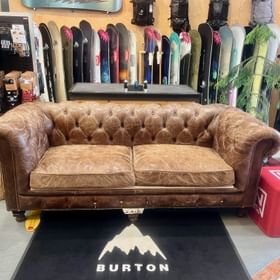 Ein braunes Ledersofa steht im Peep Shop vor einer großen Auswahl an Snowboards
