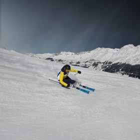 Eine Skifahrerin carved auf der Piste mit Stöckli Ski. Im Hintergrund ist ein winterliches Bergpanorama