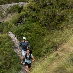 Eine Frau und ein Mann laufen in On Bekleidung und Schuhen einen Trail in Serfaus mit den Bergen im Hintergrund