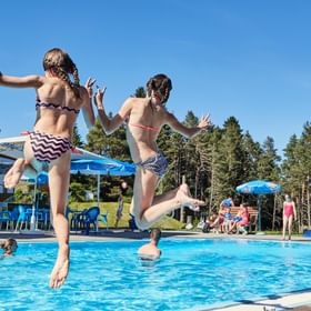 Zwei Mädchen springen vom Beckenrand in den Pool