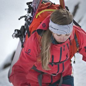 Eine Frau geht mit einem ABS Lawinenrucksack eine Bergtour in weiß verschneiten Bergen hinauf