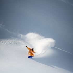 Ein Mann fährt in verschneiter Berglandschaft im Tiefschnee mit einem Snowboard 