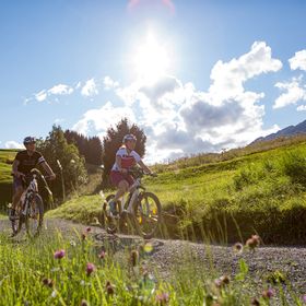 Eine Frau und ein Mann sitzen auf ihren E-Fully Mountainbikes mit Helm und Oakley Sonnenbrille auf und schauen in die Berglandschaft von Serfaus