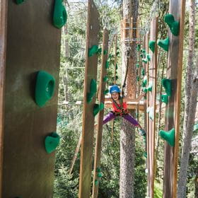 A girl climbs along a hanging climbing wall in X-Trees