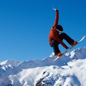 Ein Snowboarder springt über ein Gap und macht dabei einen Grap im Funpark von Serfaus