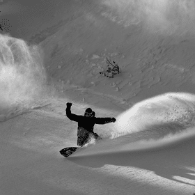 Ein Snowboarder macht mit seinem Snowboard im tiefen Schnee im Gelände einen riesigen Spray