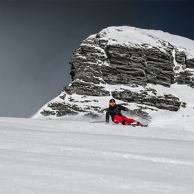 Ein Skifahrer carved auf der Piste mit Stöckli Ski. Im Hintergrund ist ein winterliches Bergpanorama