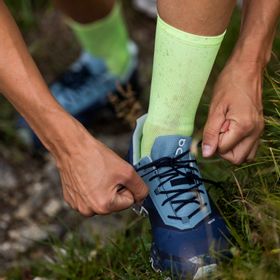 Eine Frau macht die Schnürbänder der On Cloud Running Schuhe auf einem Trail in den Bergen in Serfaus zu