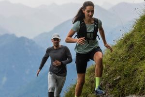 Eine Frau und ein Mann laufen in On Bekleidung und Schuhen einen Trail in Serfaus mit den Bergen im Hintergrund