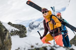 Zwei Frauen gehen eine Tour einen Berg hinauf, die Ski sind am Rucksack befestigt