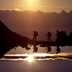 Eine Gruppe von Wanderern wandert im Sonnenaufgang am Bergsee am Furgler vorbei