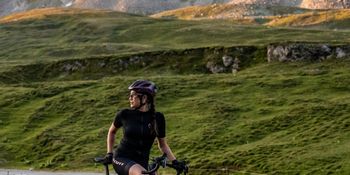 Eine Rennradfahrerin steht auf einer Straße mit ihrem Gravelbike in einer Berglandschaft