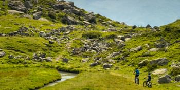 Ein Mann und eine Frau fahren auf Scott E-Bikes einen Trail in hügeliger Landschaft entlang