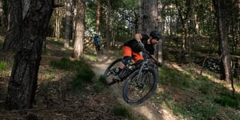 Ein Mann fährt auf einem Fully E-MTB von Scott einen Bergtrail durch den Wald hinunter 