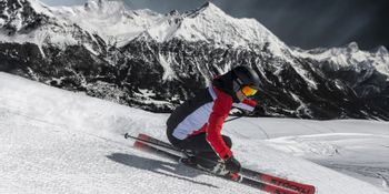Ein Mann carved auf der Piste mit Stöckli Ski. Im Hintergrund ist ein winterliches Bergpanorama