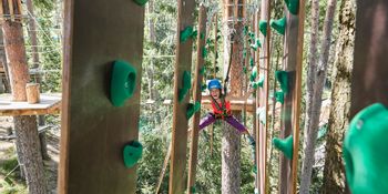 Ein Mädchen klettert entlang der hängenden Kletterwand im X-Trees