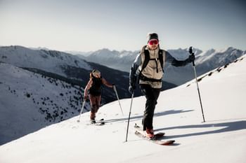 Eine Frau und ein Mann gehen mit Tourenski einen Berg bei bestem Wetter hinauf.