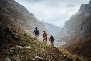 Eine Gruppe von Wanderern läuft in Scott Outdoor Bekleidung eine Wiese in einer rauen Berglandschaft