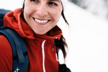 Eine Frau in Winterbekleidung der Marke Ortovox lächelt in die weisse Berglandschaft. 