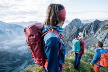 Eine Gruppe steht ausgestattet mit Wanderbekleidung von Ortovox an einem Berggrat und Blicken in das Bergpanorama mit hohen Gipfeln