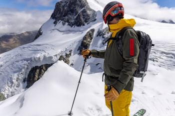 Ein Mann steht am Grat eines verschneiten Gipfels auf Ski und blickt in die Berglandschaft