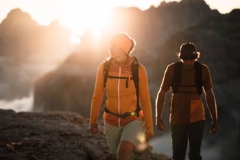 Eine Frau und ein Mann wandern im Sonnenuntergang in Ortovox Bekleidung in einer alpinen Bergwelt