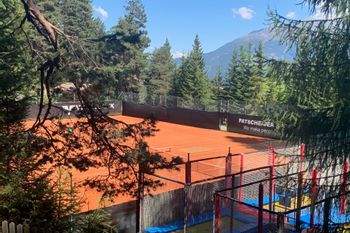 Der Tennisplatz in Serfaus umgeben von Bäumen mit toller Aussicht in die umliegende Bergwelt