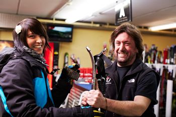 Ein freundlicher Mitarbeiter überreicht einer Kundin die Ski aus dem Depot im Check In Serfaus