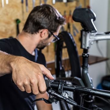 Ein Mitarbeiter kontrolliert fachmännisch die Einstellung der Bremsen bei einem Mountainbike in einer Fahrradwerkstatt