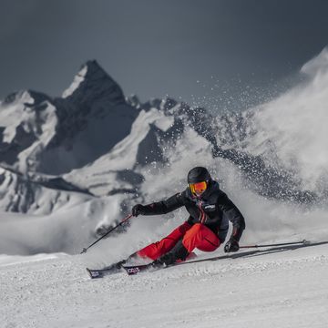 Ein Skifahrer carved auf der Piste mit Stöckli Ski. Im Hintergrund ist ein winterliches Bergpanorama