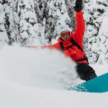 Ein Snowboarder fährt in pulvrigen Tiefschnee in einem tiefverschneiten Wald mit einem Burton Powderboard und macht einen Spray