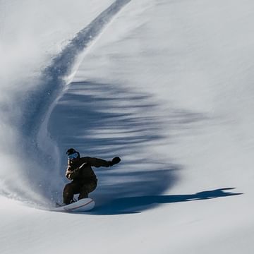 Mark Morris hinterlässt eine tiefe Spur im Powder auf einem Burton Snowbaord in einem Tiefschnee Berghang