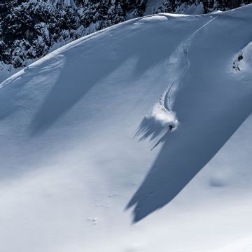 Ein Freerider fährt im tiefen Pulverschnee einen steilen Hang am Berggrat hinunter