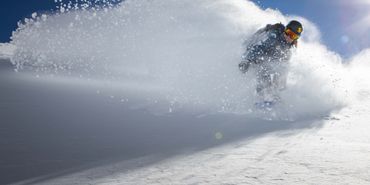Eine Snowboarderin fährt im Tiefschnee durch eine Schneewolke